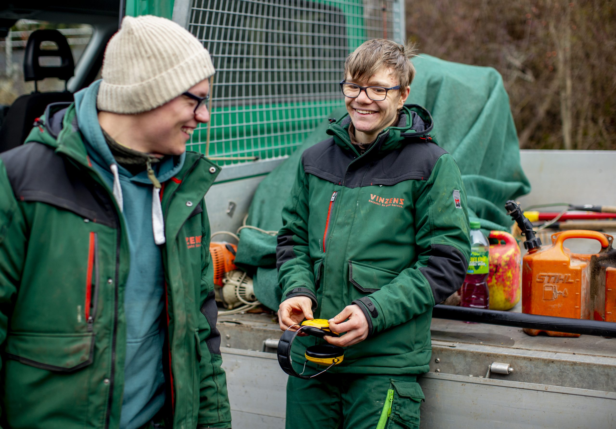 Zwei Mitarbeiter des Garten- und Landschaftsbaus vor einem Lastwagen, lachen.