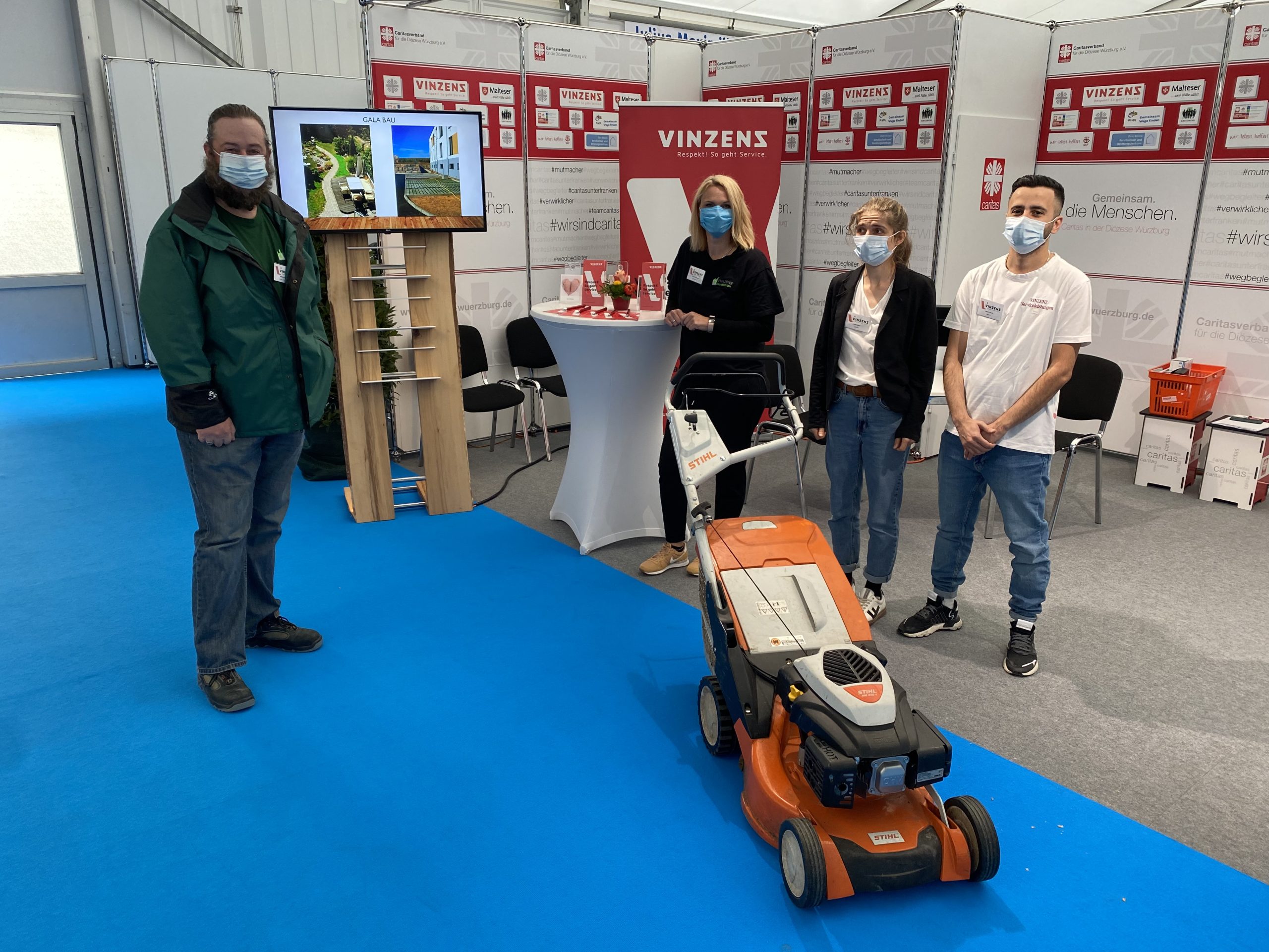 Vinzenz-Messestand mit Rasenmäher auf blauem Teppich.