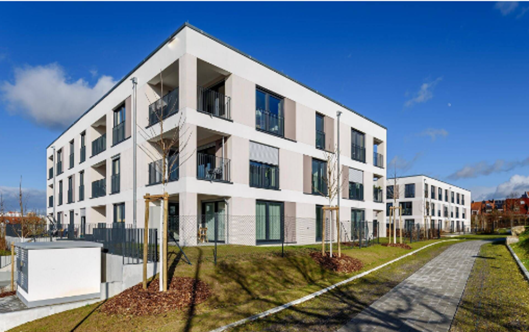 Zwei dreigeschossige, moderne Flachdachbauten neben einem Fußweg im Neubaugebiet.