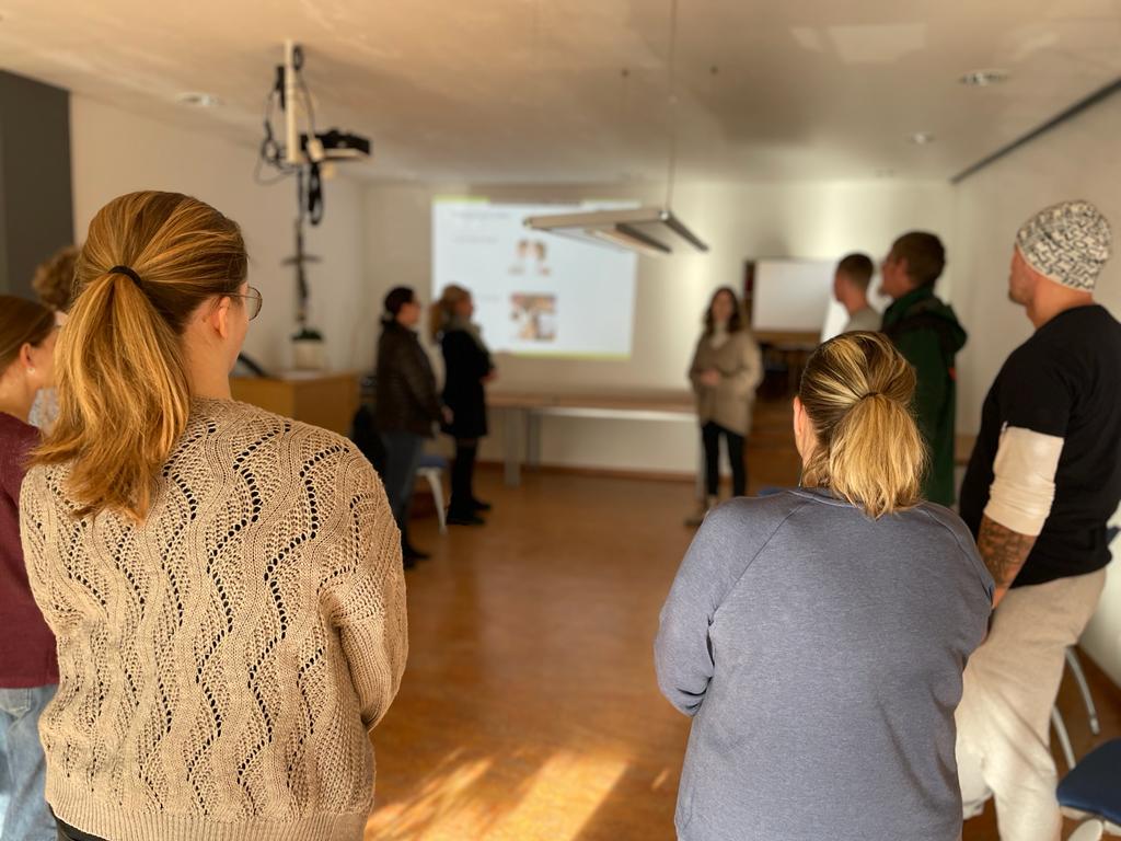 Das Foto zeigt die Teilnehmer:innen im Schulungsraum der Vinzenz Werke Würzburg. Eine der beiden Organisatorinnen erklärt gerade etwas zum Thema gewaltfreie Kommunikation.