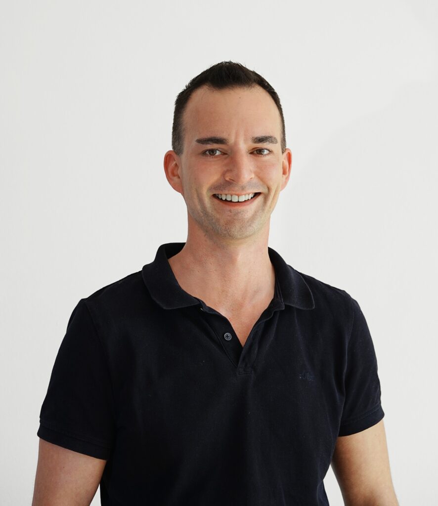 Portrait von Michael Herrmann. Er trägt ein schwarzes Polo-Shirt, hat kurzgeschnittenes braunes Haar und lächelt offen in die Kamera.