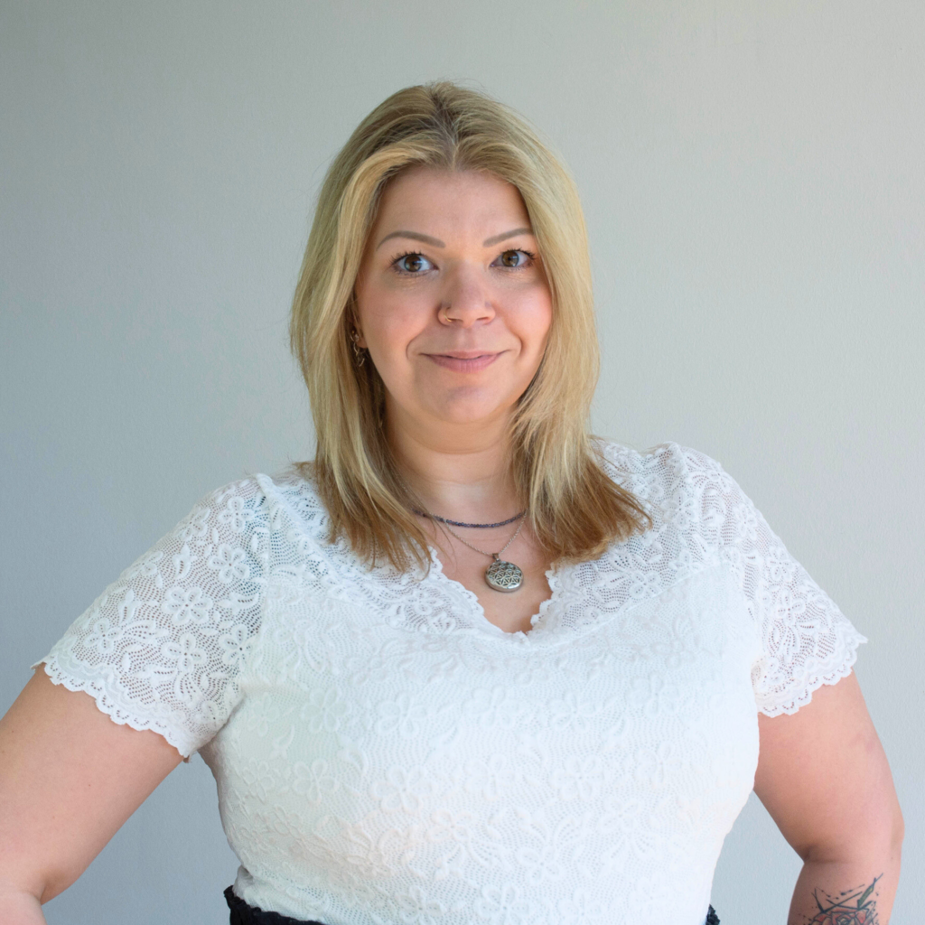 Portraitbild von Katja Bildner. Sie lächelt in die Kamera. Blonde, schulterlange Haare, weiße Bluse