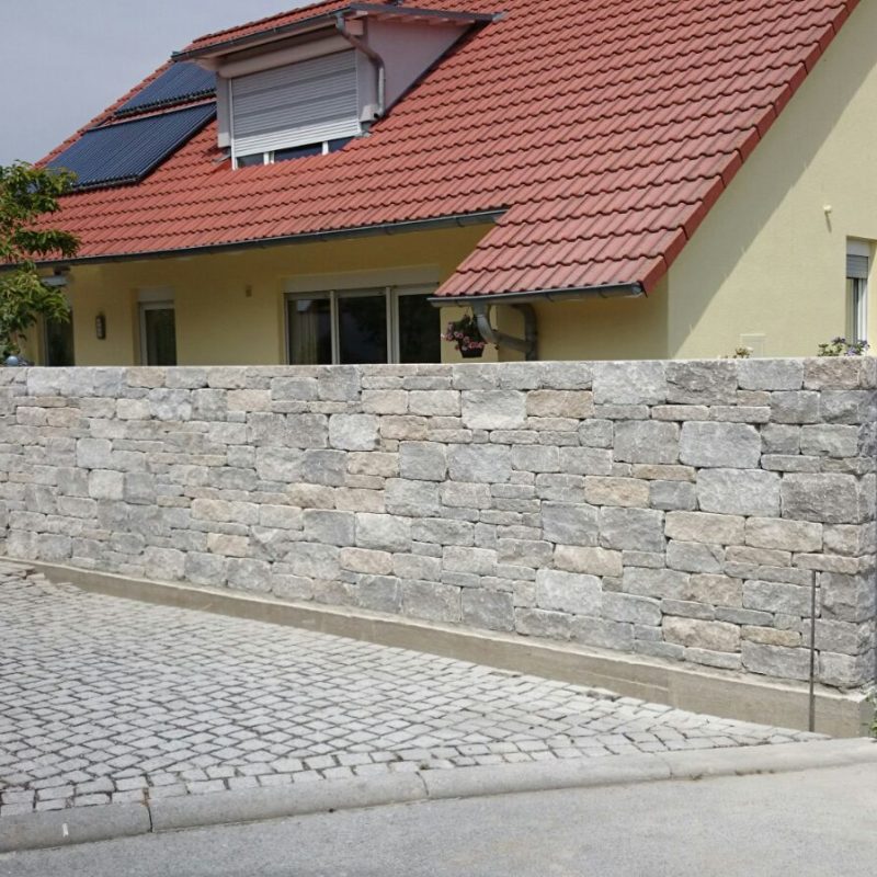 Mauer aus Natursteinen um ein Einfamilienhaus.