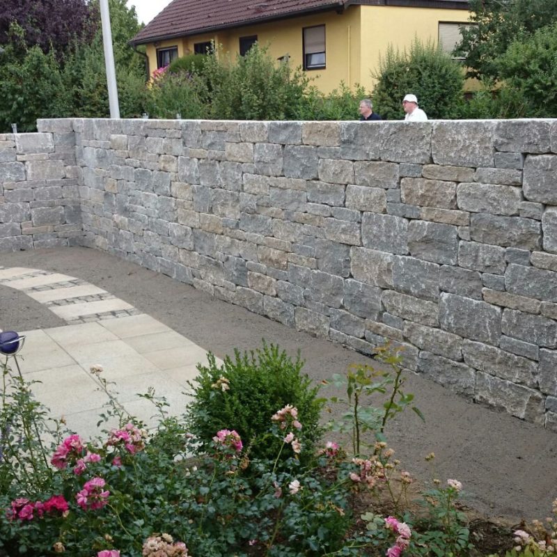 Mauer aus Natursteinen um ein Einfamilienhaus.