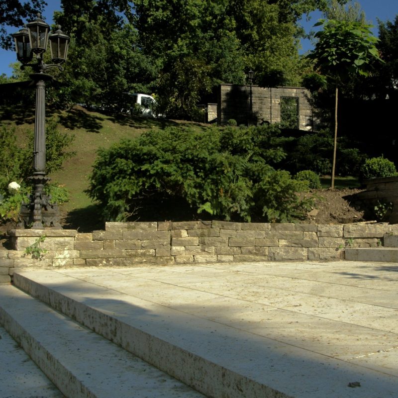 Gemauerter Platz mit Treppen vor einem Park.